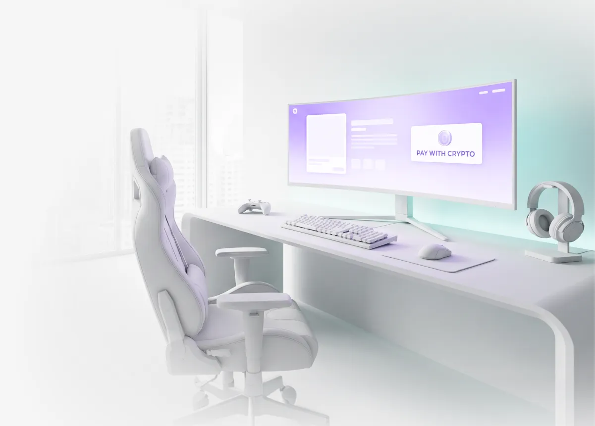 A white gaming desk with an ultrawide monitor showing a “Pay with crypto” checkout button