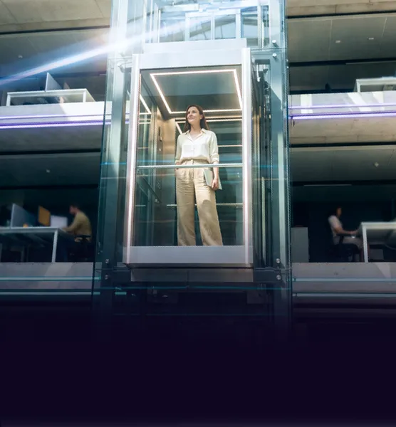 A woman in a glass lift rising through a modern office building at night