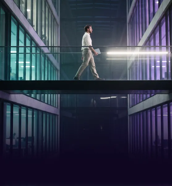 A man crossing a lit glass walkway between two office towers
